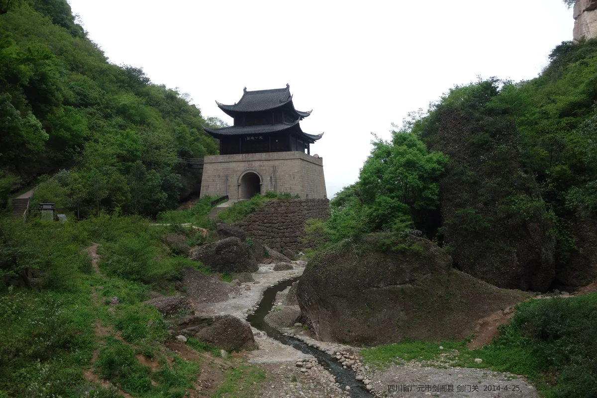 剑门关景区关楼与两侧绿树山壁，前景为石溪。照片摄于2014年，不是古道步行路段，不包含在三日主行程内，也不代表当前路况。